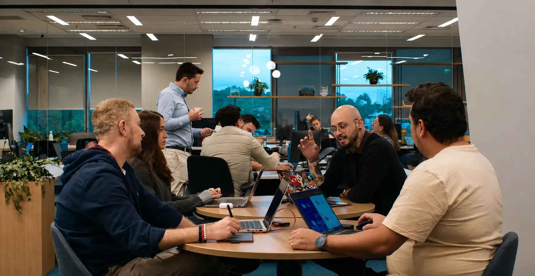 Equipe reunida em mesa de trabalho colaborativo com notebooks abertos, em escritório moderno