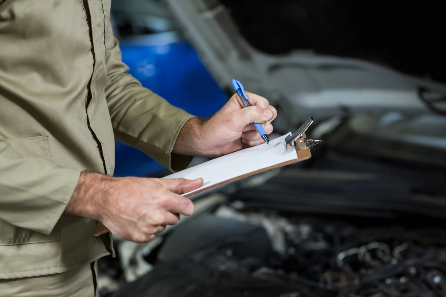 Inspector notes an assessment on a clipboard in front of a car's open hood