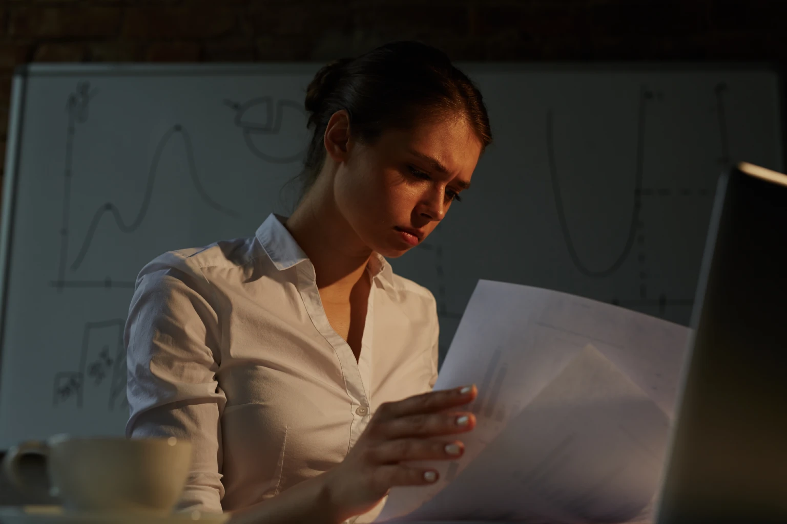 Mulher analisando documentos com atenção em um escritório com pouca iluminação