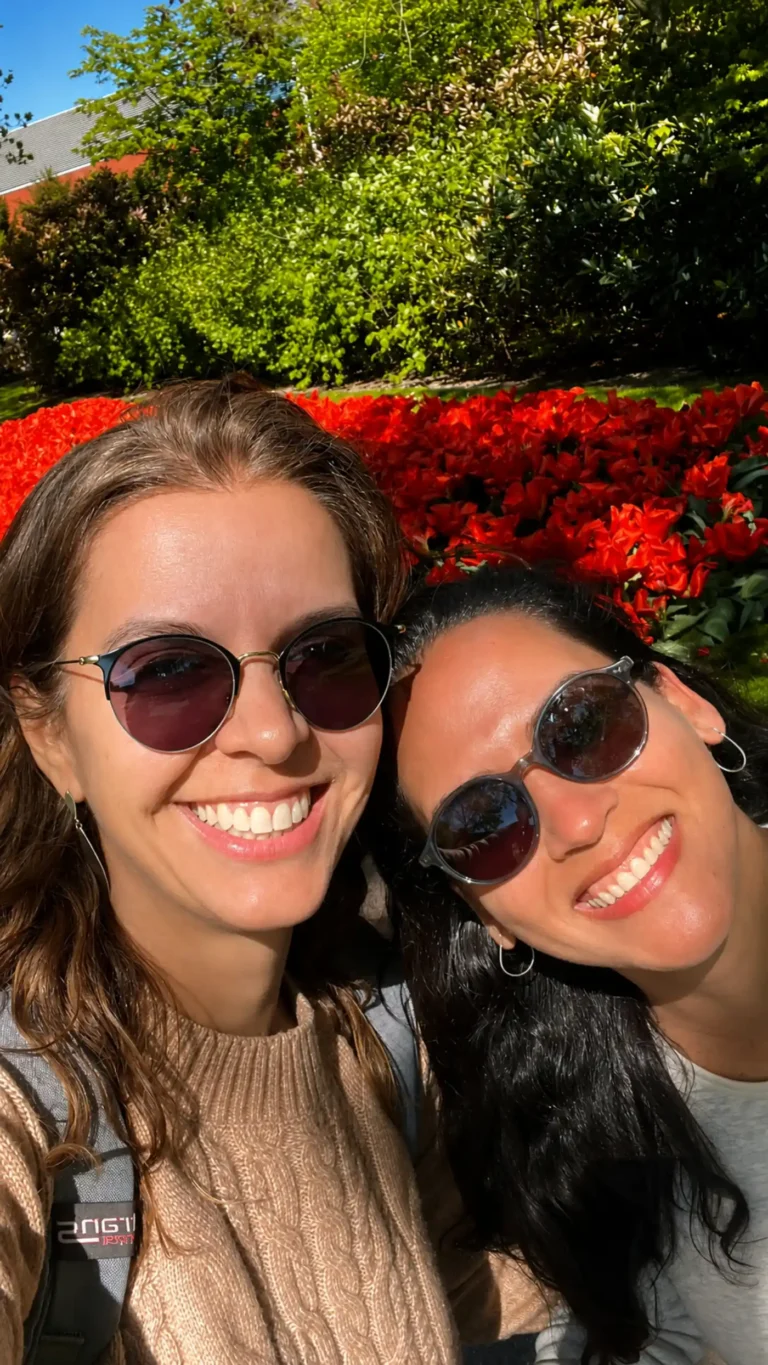 Renata Capucci sorrindo ao lado da esposa em um jardim florido